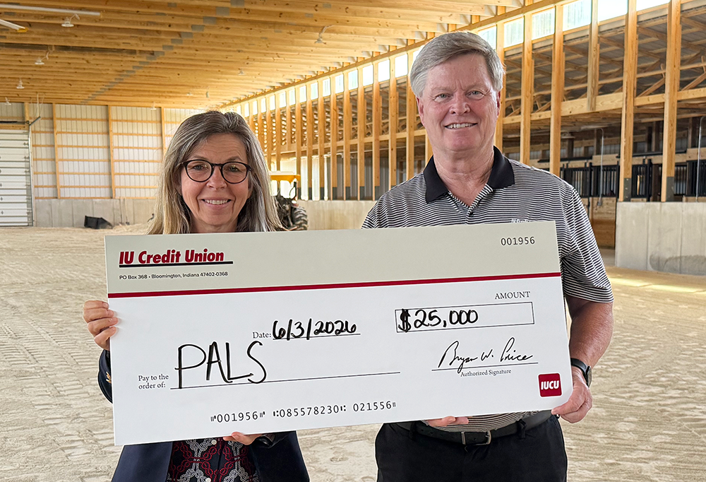 PALS Executive Director Christine Herring and IU Credit Union President and CEO Bryan Price hold a $25,000 donation check inside a barn under construction.
